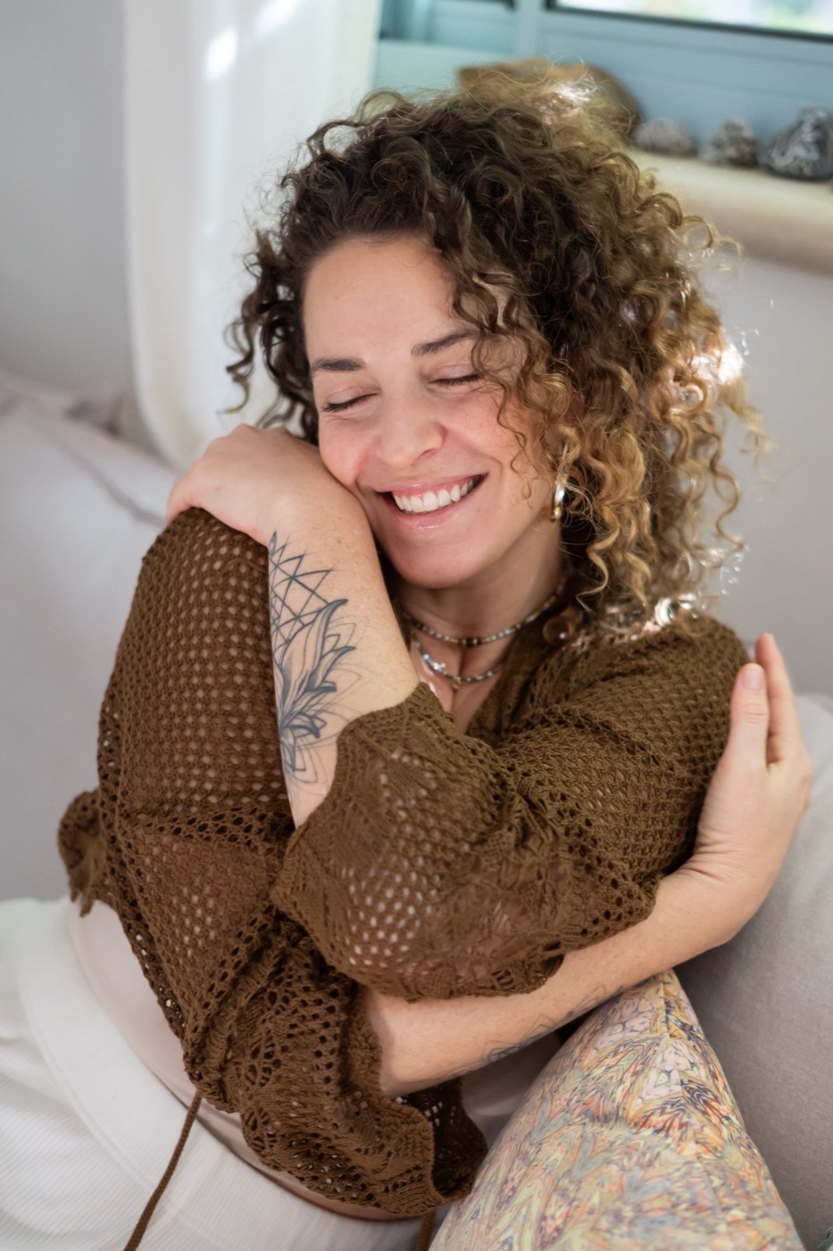 Idit smiling with her eyes closed, hugging her own shoulders
